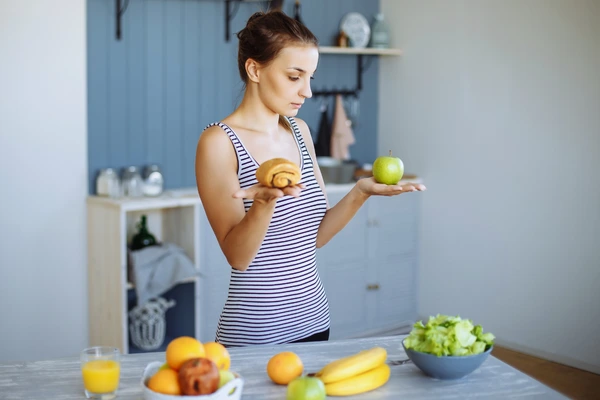 Woman choosing between a pastry and an apple—diet choices affect allergy, weight loss and cravings